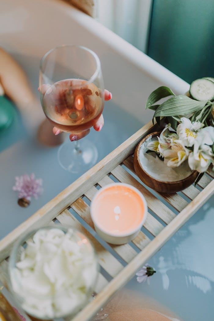 About A serene bath setting with wine, candles, and flowers for a relaxing spa experience.